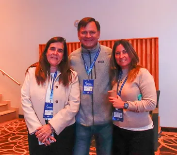 Tres participantes sonriendo frente al escenario del 6.º Encuentro